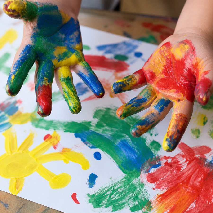 Two hands covered in bright poster paint, over a painted sheet of paper